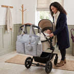 Quilted changing bag tote with a bottle in the side pocket, next to a pram with baby