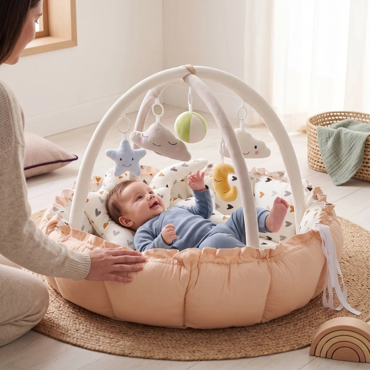 Baby playing under the hanging toys in the peach play gym nest, with a parent beside them