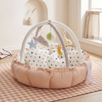 Peach baby play gym nest on a checked rug with soft hanging toys