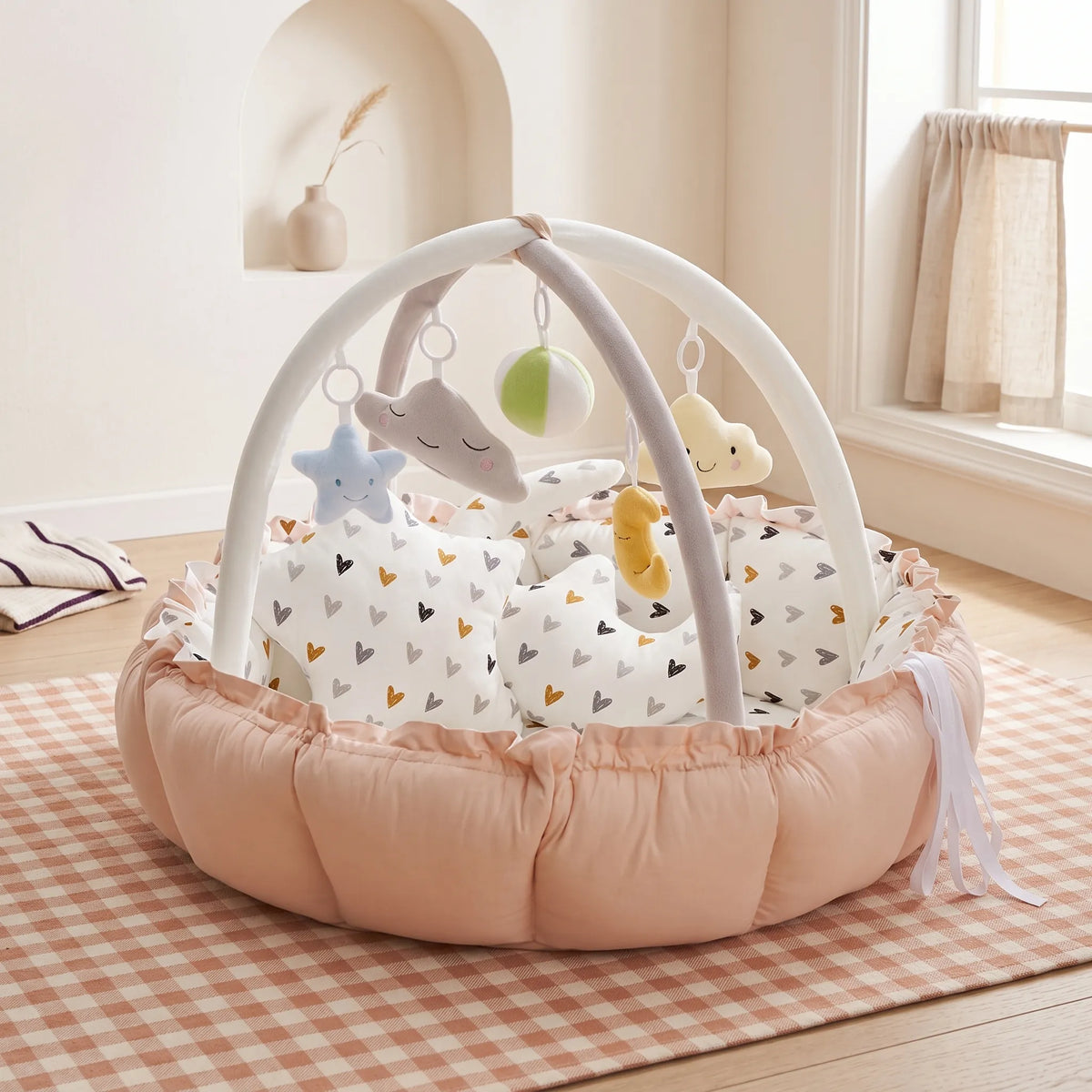 Peach baby play gym nest on a checked rug with soft hanging toys