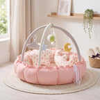 Pink baby play gym nest with heart print cushions in a bright nursery