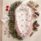 Christmas baby nest with reindeer print and pink trim, surrounded by festive greenery