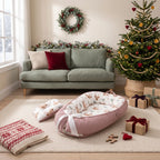 Reindeer print baby nest beside wrapped presents and a Christmas tree