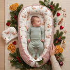 Baby in a green sleepsuit resting in the reindeer print baby nest with a parent close by