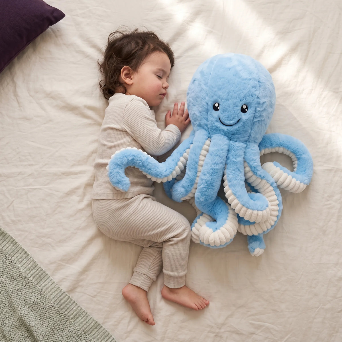 Blue octopus cuddly toy with an embroidered smile next to a resting toddler