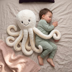 Toddler cuddled up beside a white octopus soft toy on a bed