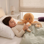 Smiling child in bed holding the curly tentacle of a peach octopus cuddly toy