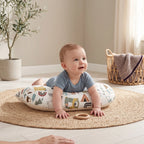 Happy baby on their tummy on the Jungle tummy time pillow, with a parent's hand nearby