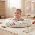 Baby lifting their head during tummy time on the U-shaped pillow, on a nursery rug