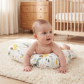 Smiling baby on their tummy on the Green Dinosaur tummy time pillow