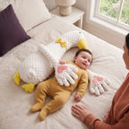 Smiling baby in a mustard sleepsuit with the duck patting pillow's soft hands on their tummy, parent close by