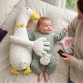 Baby lying on their back beside the white duck patting pillow, with a parent holding the remote