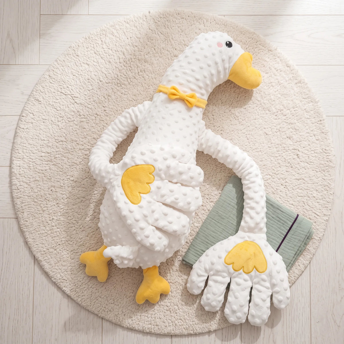White duck patting pillow with a yellow beak and long huggable arms on a cream rug